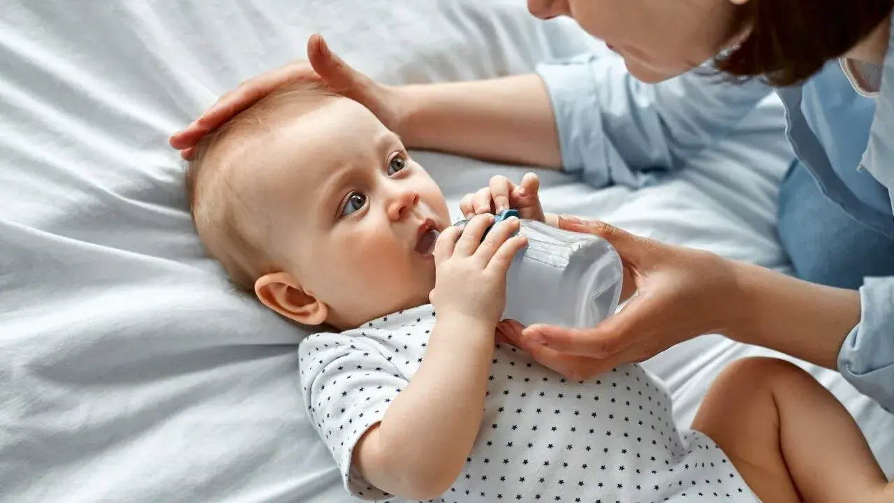 Maluch szarpie się przy karmieniu butelką, ale mama cierpliwie go uspokaja.