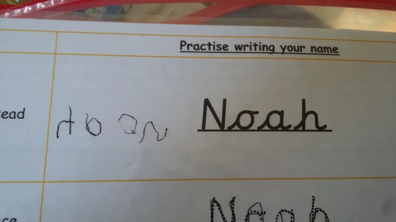 Siedmiolatek ćwiczy pisanie imienia "Noah" w lustrzanym odbiciu. Obok widać próbę pisania imienia.