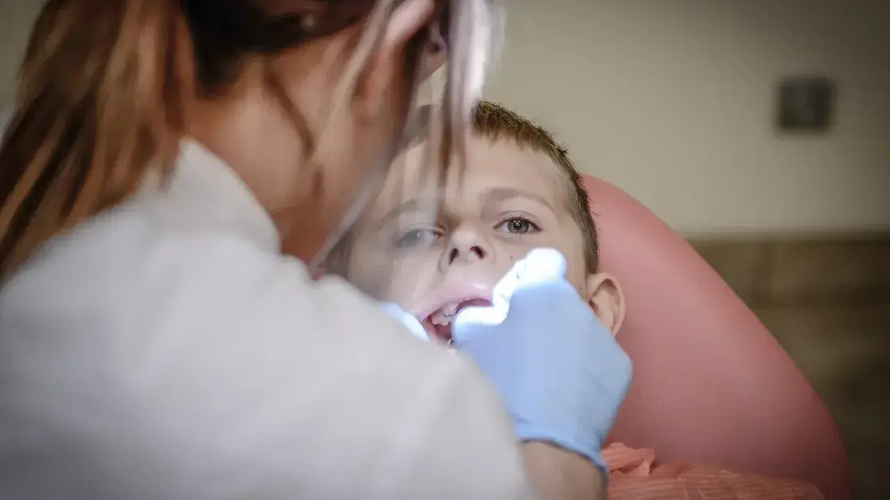 Chłopiec nie chce otworzyć ust u dentysty. Stomatolog próbuje go zbadać.