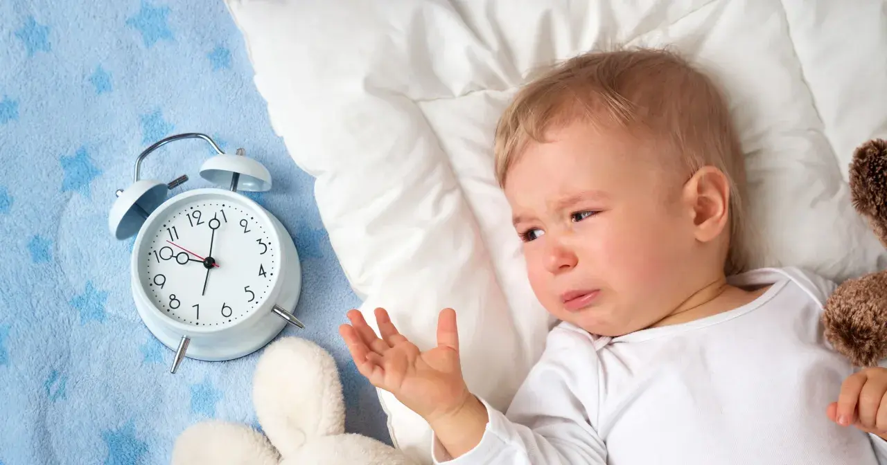 Płacz 1,5 rocznego dziecka, które nie chce spać w dzień. Obok budzik i pluszaki.