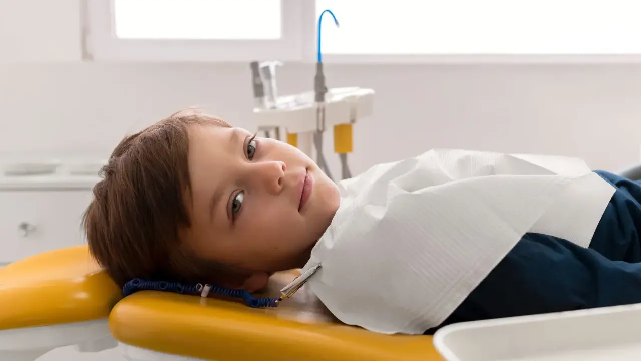 Chłopiec leży na żółtym fotelu dentystycznym, przygotowany do leczenia zębów pod narkozą.