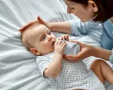 Maluch szarpie się przy karmieniu butelką, ale mama cierpliwie go uspokaja.