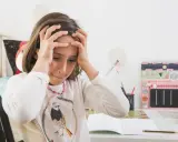 Dziewczynka z rękami na głowie, zmartwiona nauką. Jak rozładować stres u dziecka? Może przerwa na zabawę?