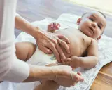 Rąk opiekuna zmienia pieluszkę niemowlęciu. Czy to powód, dlaczego 2 miesięczne dziecko nie sika w nocy?