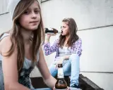 Dwie nastolatki piją piwo, co może być początkiem alkoholizmu wśród młodzieży.
