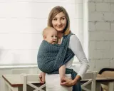 Uśmiechnięta mama nosi dziecko w chuście tkanej, która zapewnia komfort i bezpieczeństwo.