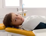 Chłopiec leży na żółtym fotelu dentystycznym, przygotowany do leczenia zębów pod narkozą.