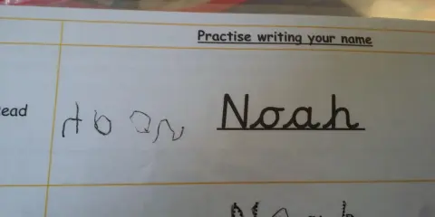 Siedmiolatek ćwiczy pisanie imienia "Noah" w lustrzanym odbiciu. Obok widać próbę pisania imienia.
