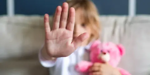 Dziecko z pluszowym misiem pokazuje dłoń na znak stopu, jakby chciało uniknąć klapsa w pupę.