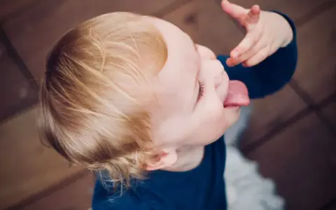 Małe dziecko nie słucha w przedszkolu, wyciąga język i bawi się jedzeniem.