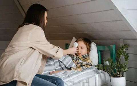 Mama mierzy gorączkę choremu dziecku, szukając domowych sposobów na zapalenie krtani u dziecka.