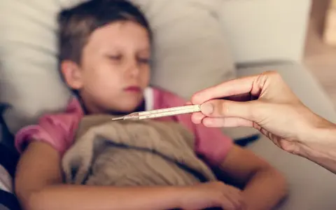 Dziecko z gorączką, czuć zimne rączki i nóżki. Mama mierzy temperaturę termometrem.