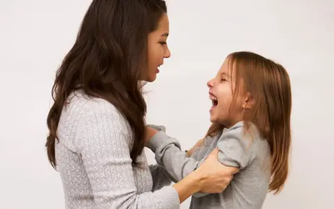 Mama śmieje się, łapiąc córkę za ręce. Dziecko radośnie szarpie się w nerwach, śmiejąc się głośno.