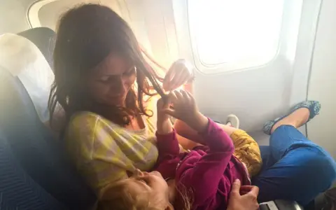 Ciepłe chwile w samolocie: mama bawi się włosami swojego dziecka, które leży na jej kolanach.