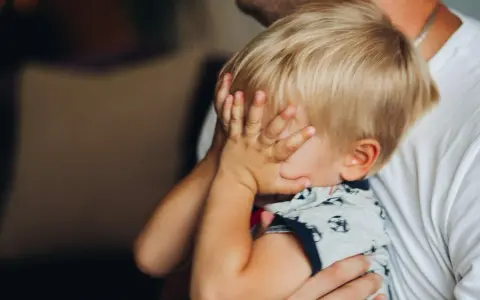 2,5-letnie dziecko budzi się w nocy z płaczem, ukrywając twarz w dłoniach. Tata tuli go, próbując uspokoić.