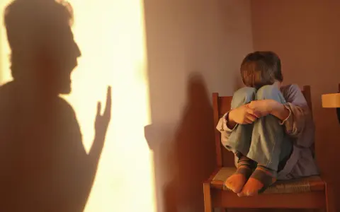 Cień ojca krzyczy, a dziecko skulone na krześle czuje się przytłoczone.