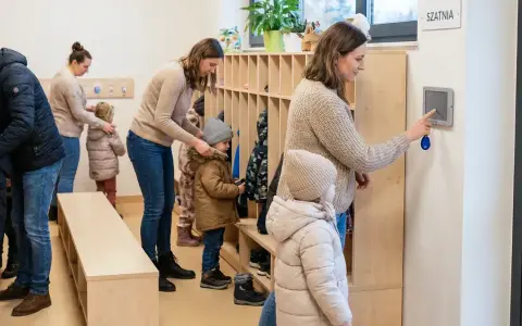 Rodzice odbierają dzieci z przedszkola. W szatni panuje ruch, dzieci ubierają się do wyjścia.