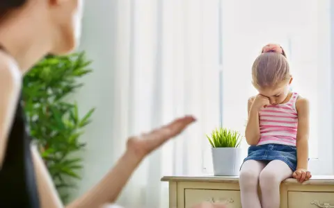 Smutna dziewczynka siedzi przy oknie, a jej mama gestykuluje. Warto nauczyć się, jak przestać krzyczeć na dziecko, by budować lepsze relacje.