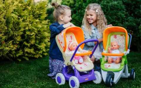 Dwie dziewczynki bawią się lalkami w wózkach, odgrywając różne etapy życia dziecka.