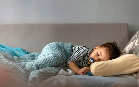 Małe dziecko śpi na kanapie, otulone kocykiem. Czy to już czas, kiedy dziecko przestaje mieć drzemki?