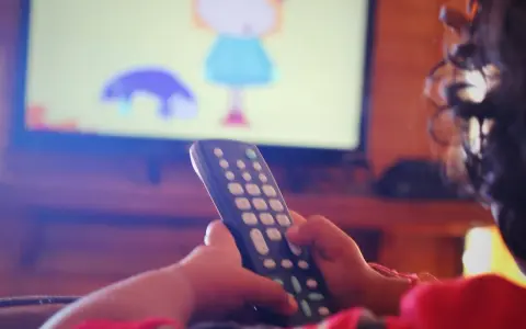 Dziecko z pilotem w ręku ogląda bajkę na telewizorze w pokoju.