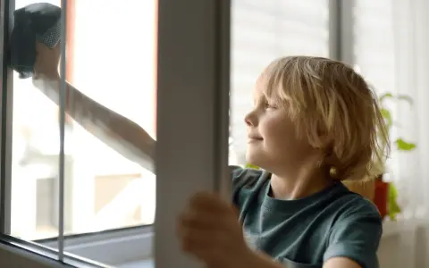 Chłopiec z uśmiechem na twarzy wykonuje jedno z domowych obowiązków – myje okno.