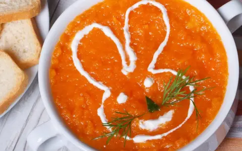 Pomarańczowa marchwianka z ryżem na biegunkę, ozdobiona śmietaną w kształcie królika. Podana z grzankami.