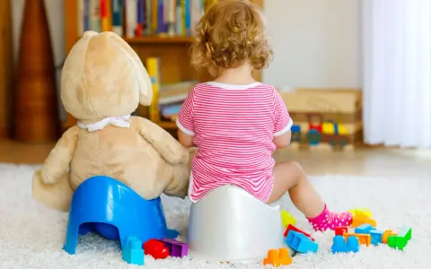 Dziecko siedzi na nocniku, obok pluszowy miś. Wokół klocki. Może to być psychiczna blokada przed wypróżnieniem.