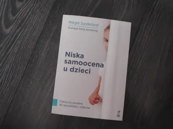 Książka "Niska samoocena u dzieci" Margot Sunderland. Na okładce fragment twarzy dziecka ukrywającego się za białą zasłoną.